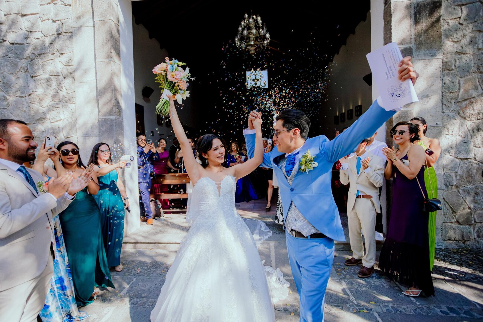 Novios celebrando entre aplausos y confeti al salir de la ceremonia